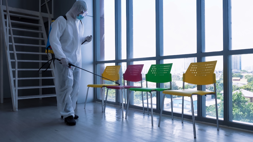 Worker in personal protective equipment (ppe) suit cleaning in building with spray disinfectant water to remove covid 19